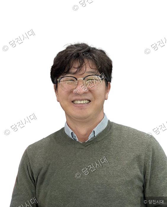 안경을 쓴 남성이 밝게 미소 지으며 카메라를 바라보고 있다.