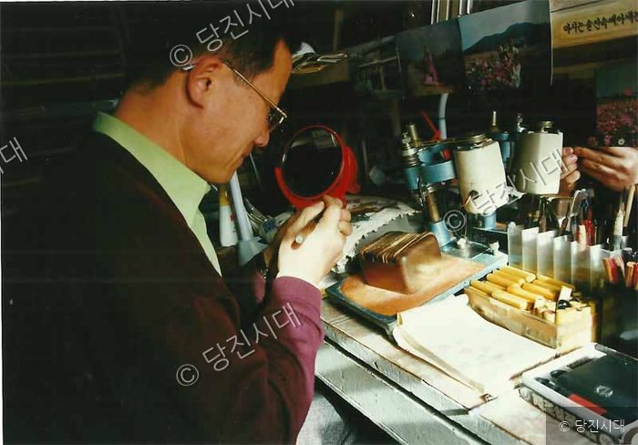 한 남성이 작업실에서 집중하여 세공 작업을 하고 있다.