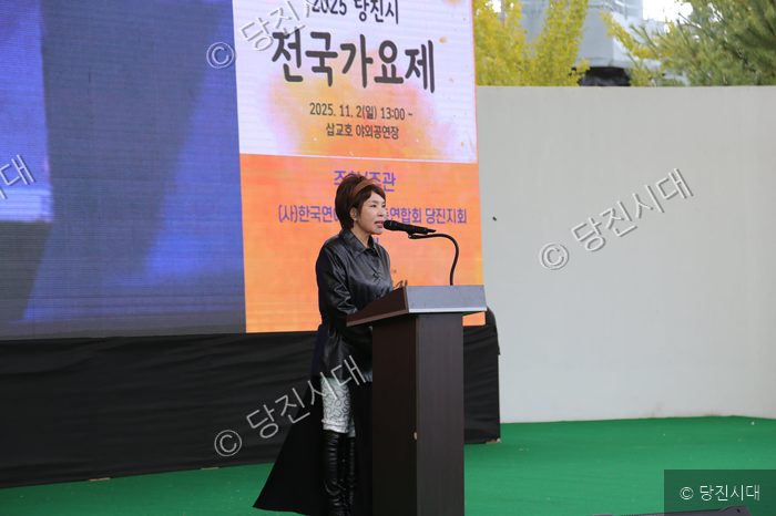 한 여성이 무대 연상에서 마이크를 잡고 발언하고 있다.