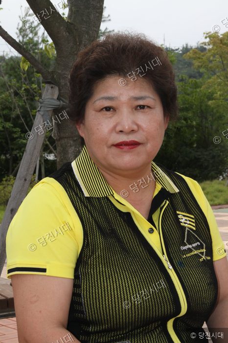 노란색 의상을 입은 신출균 대표이사가 야외에서 포즈를 취하고 있다.