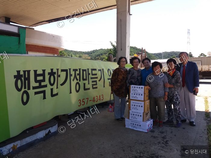 주민들이 행복한가정만들기운동 현수막 앞에서 후원물품을 들고 기념 촬영을 하고 있다.