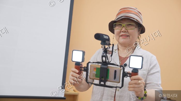 노년 여성이 스마트폰 촬영 장비를 들고 미소 짓고 있다.