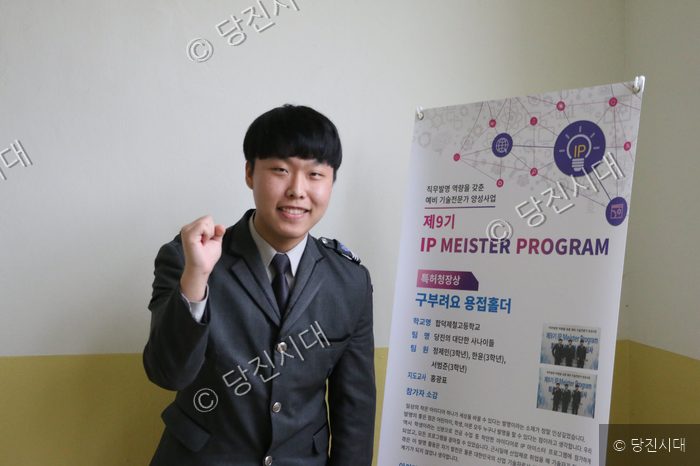 합덕제철고등학교 학생이 IP 마이스터 프로그램 포스터 옆에서 포즈를 취하고 있다.