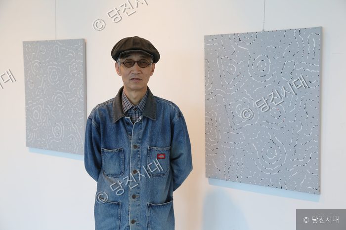 작가 한 명이 미술관에서 자신의 작품을 배경으로 서 있다.
