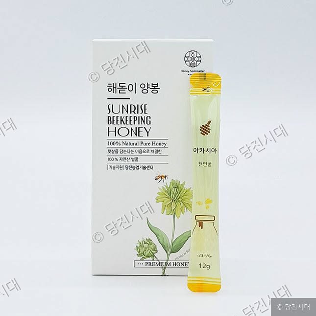해돋이양봉의 스틱형 아카시아 천연꿀 제품이 상자와 함께 놓여 있다.