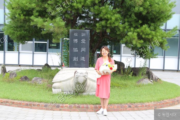 박옥진 씨가 학교 기념비 앞에서 꽃다발을 들고 포즈를 취하고 있다.