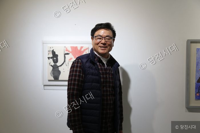 한 남성이 미술관에서 자신의 작품을 배경으로 서 있다.