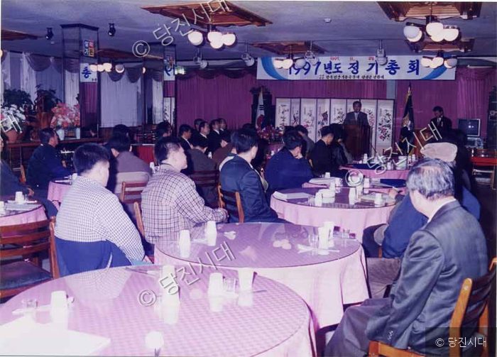 사람들이 실내 연회장에 모여 1997년도 정기총회 행사를 하고 있다.
