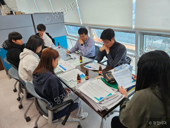 청소년들이 회의실에 모여 서류를 검토하며 의견을 나누고 있다.