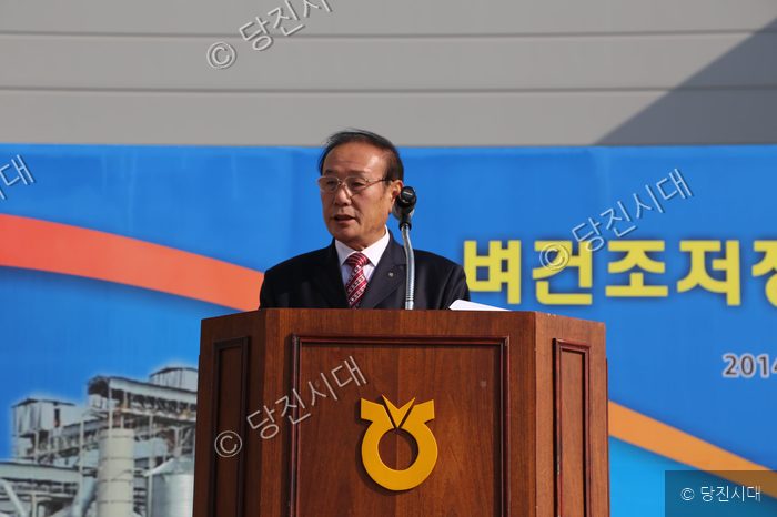 한 남성이 단상에 서서 마이크를 잡고 연설하고 있다.