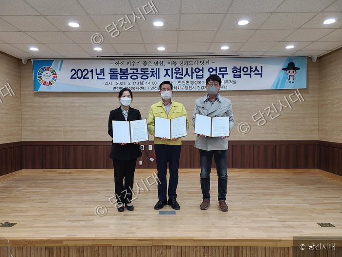 세 명의 관계자가 돌봄공동체 지원사업 업무 협약서 들고 기념 촬영을 하고 있다.