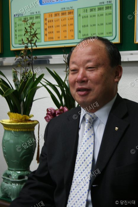 이완선 조합장이 정장을 입고 밝은 표정으로 앉아 있다.