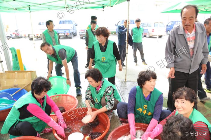 마을 주민들이 천막 아래 모여 음식을 준비하거나 설거지를 하고 있다.