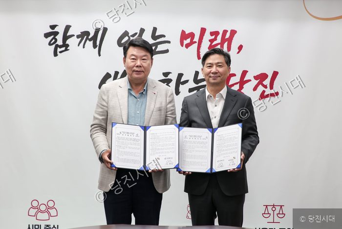 두 남성이 협약서를 들어 보이며 기념 촬영을 하고 있다.