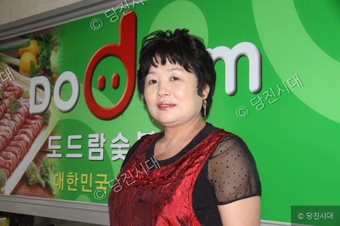 한 여성이 도드람 숯불구이 홍보물 앞에서 미소 짓고 있다.