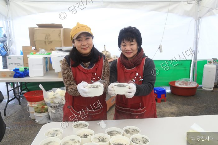 두 명의 여성이 떡국 그릇을 들고 미소를 짓고 있다.