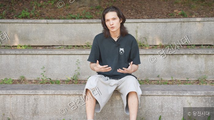 한 남성이 야외 계단에 앉아 두 손을 모은 채 이야기하고 있다.