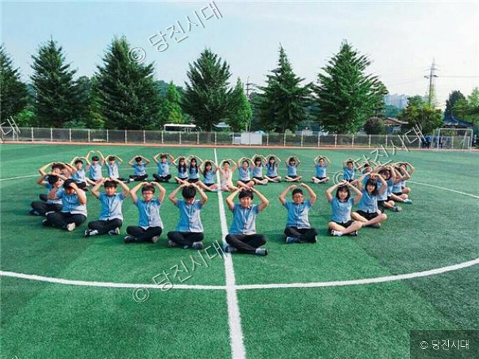 송악중학교 학생들이 운동장에 앉아 손으로 하트 모양을 만들고 있다.