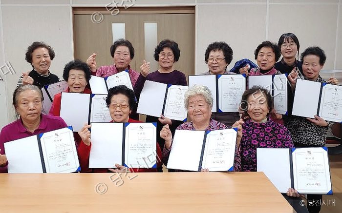 어르신들이 기억튼튼교실 수료식에서 수료증을 들고 기념 촬영을 하고 있다.