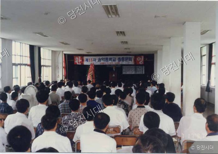 실내 강당에 모인 사람들이 행사에 참여하고 있다.