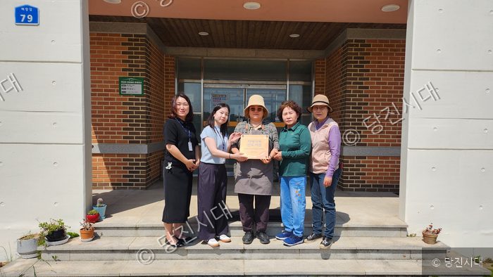 당진시보건소 관계자와 주민들이 치매극복선도기업 지정서 현판을 들고 기념촬영을 하고 있다.
