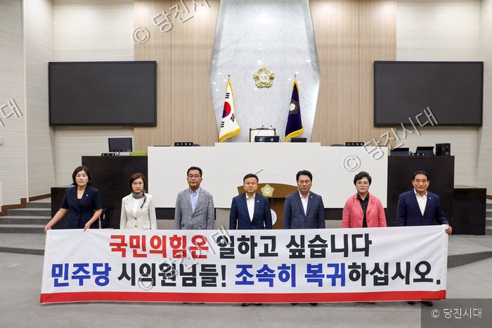 의회 본회의장에서 시의원들이 현수막을 들고 서 있다.