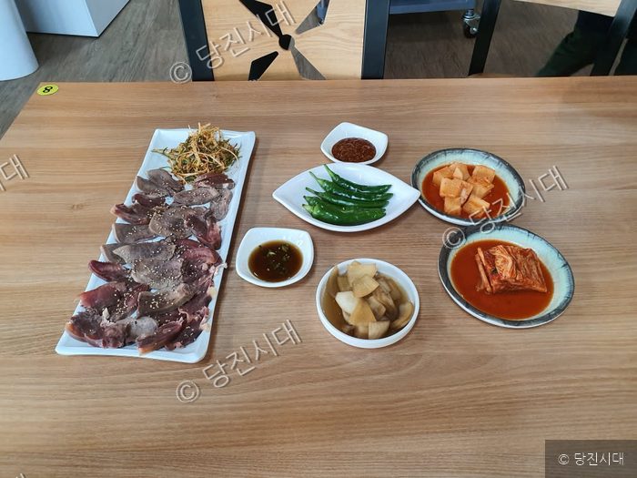 식당 테이블 위에 소머리국밥 고기 수육과 다양한 밑반찬이 차려져 있다.