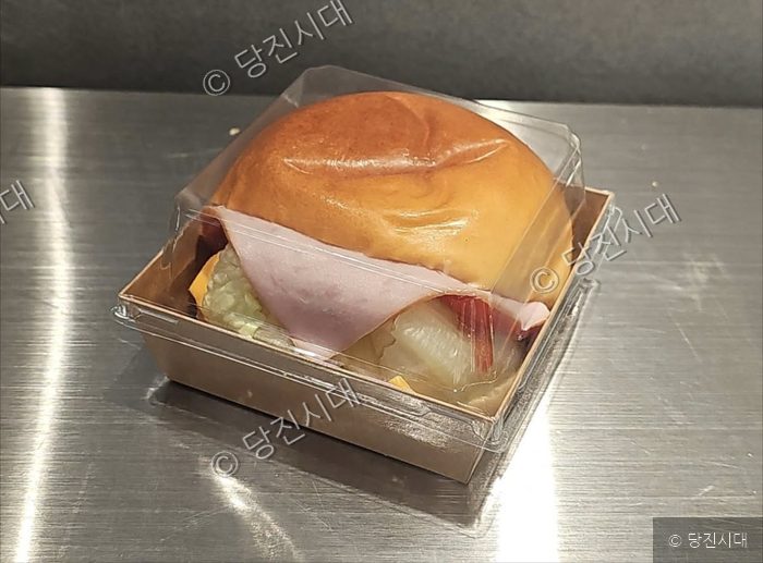 투명 용기에 담긴 햄치즈 샌드위치가 놓여 있다.