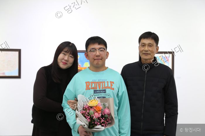 송규민 씨가 전시회에서 꽃다발을 들고 가족과 함께 기념사진을 찍고 있다.