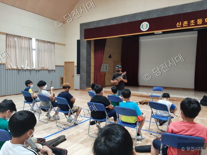 초등학생들이 강당에서 강사의 지도에 따라 우쿨렐레를 배우고 있다.