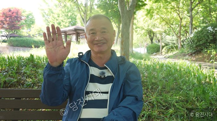 블라디미르 씨가 공원 벤치에 앉아 손을 흔들고 있다.